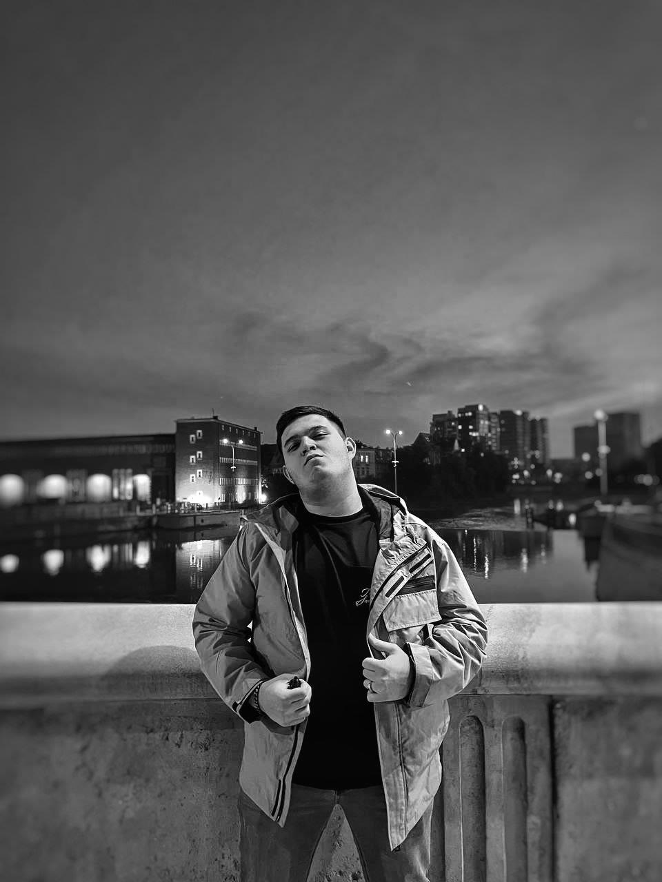 Alexander Aluf standing on a bridge at dusk, photographed in black and white